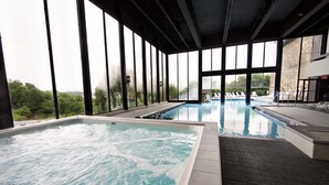 A large indoor swimming pool with clear water, surrounded by large windows offering views of greenery and a stone building. - Lodge Of Four Seasons Golf Resort, Marina & Spa (Lake Ozark)