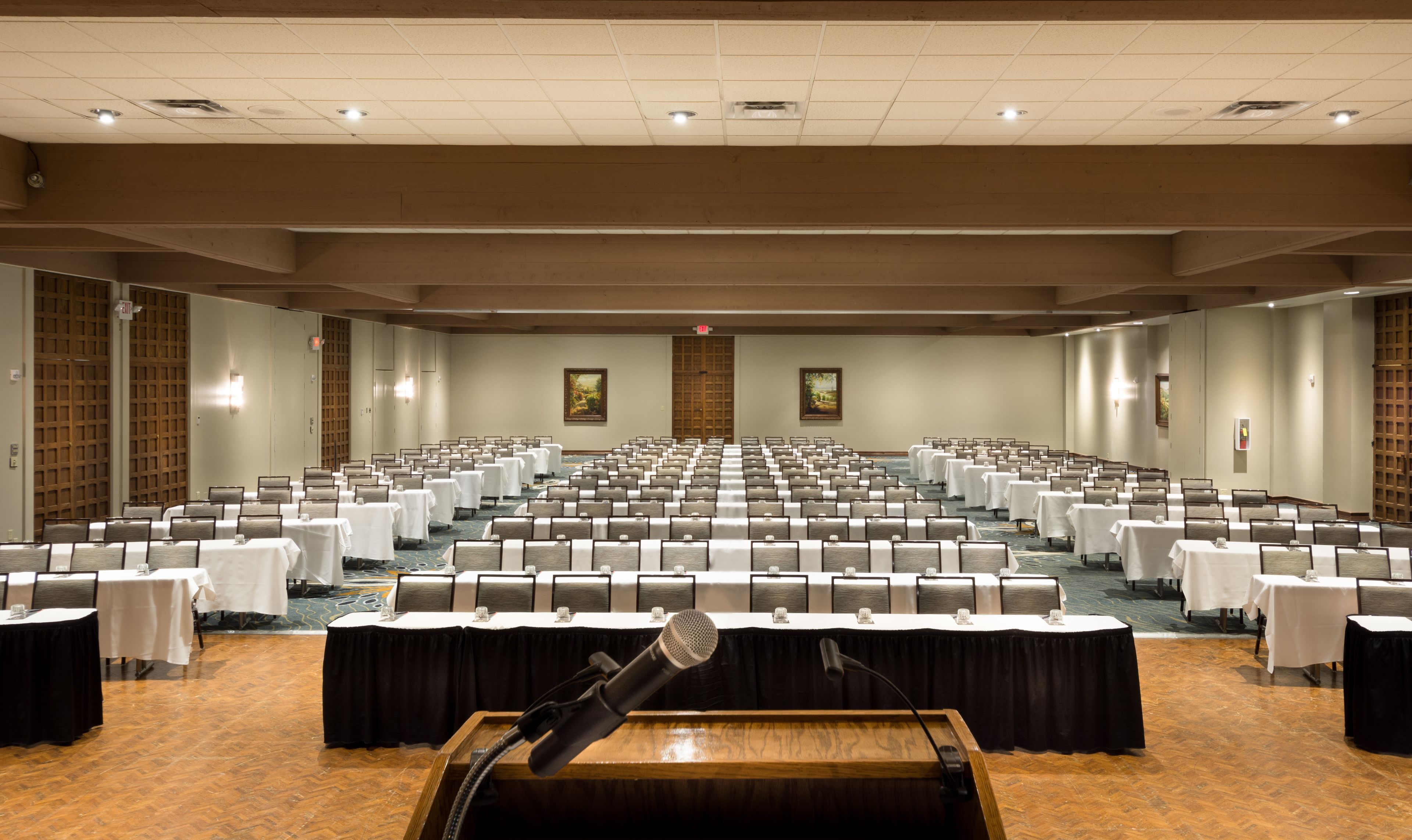 A conference room with rows of tables and chairs, a podium, and a wooden floor.
