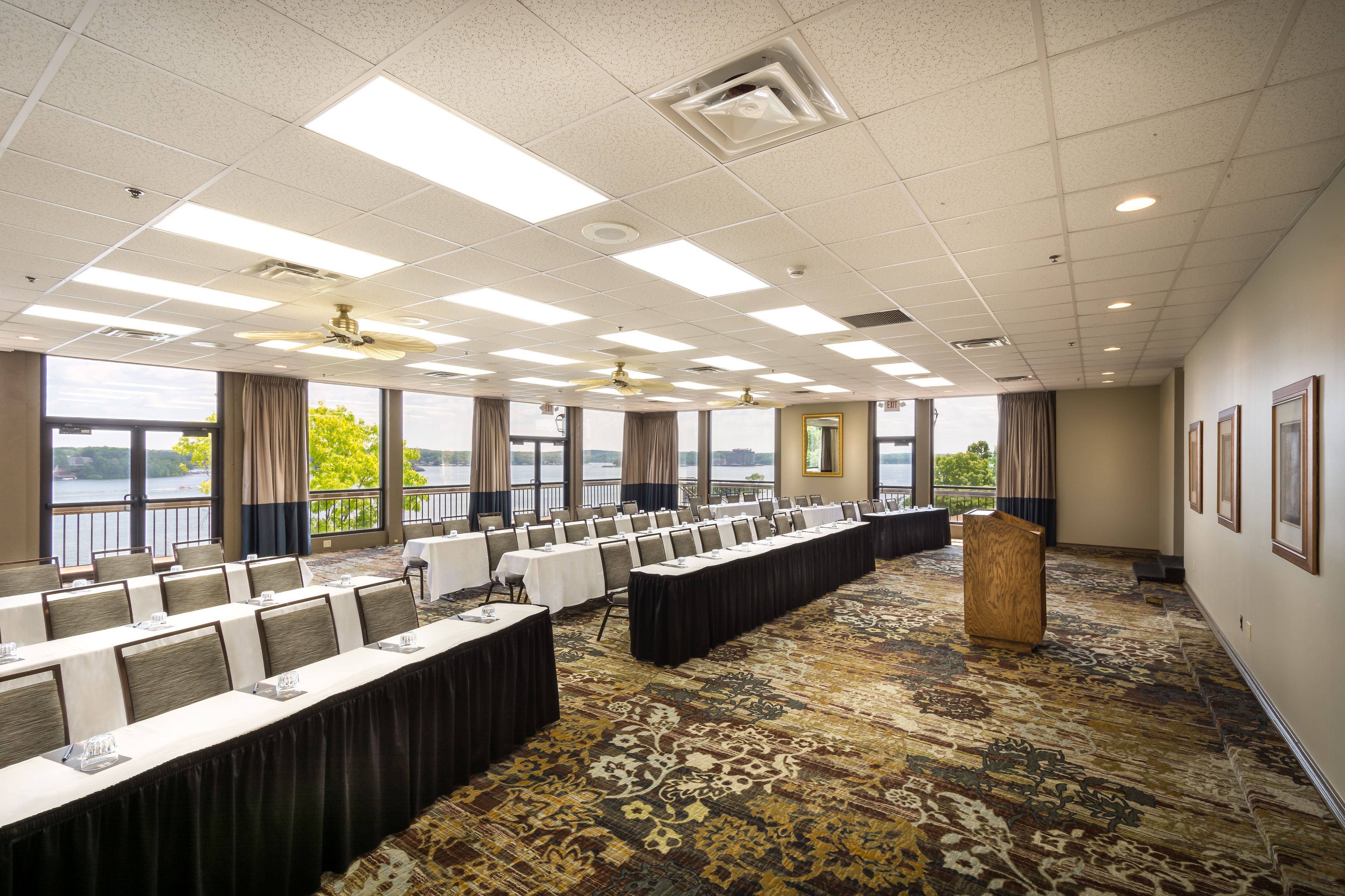 A conference room with a long table, chairs, a podium, and large windows with a view of a body of water.