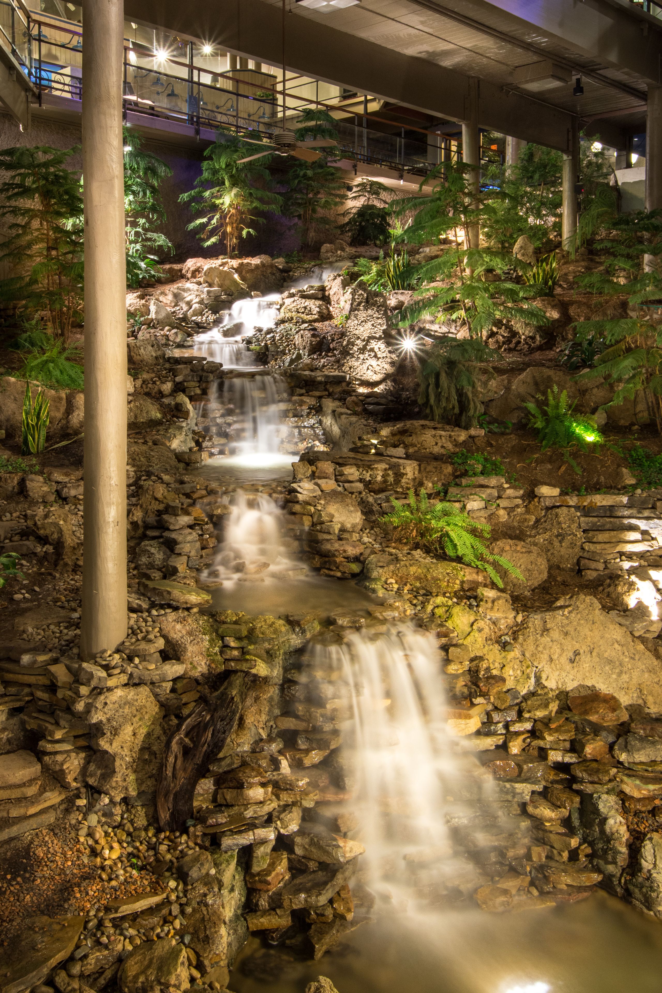 A waterfall in a landscaped area with stone structures and tropical plants.