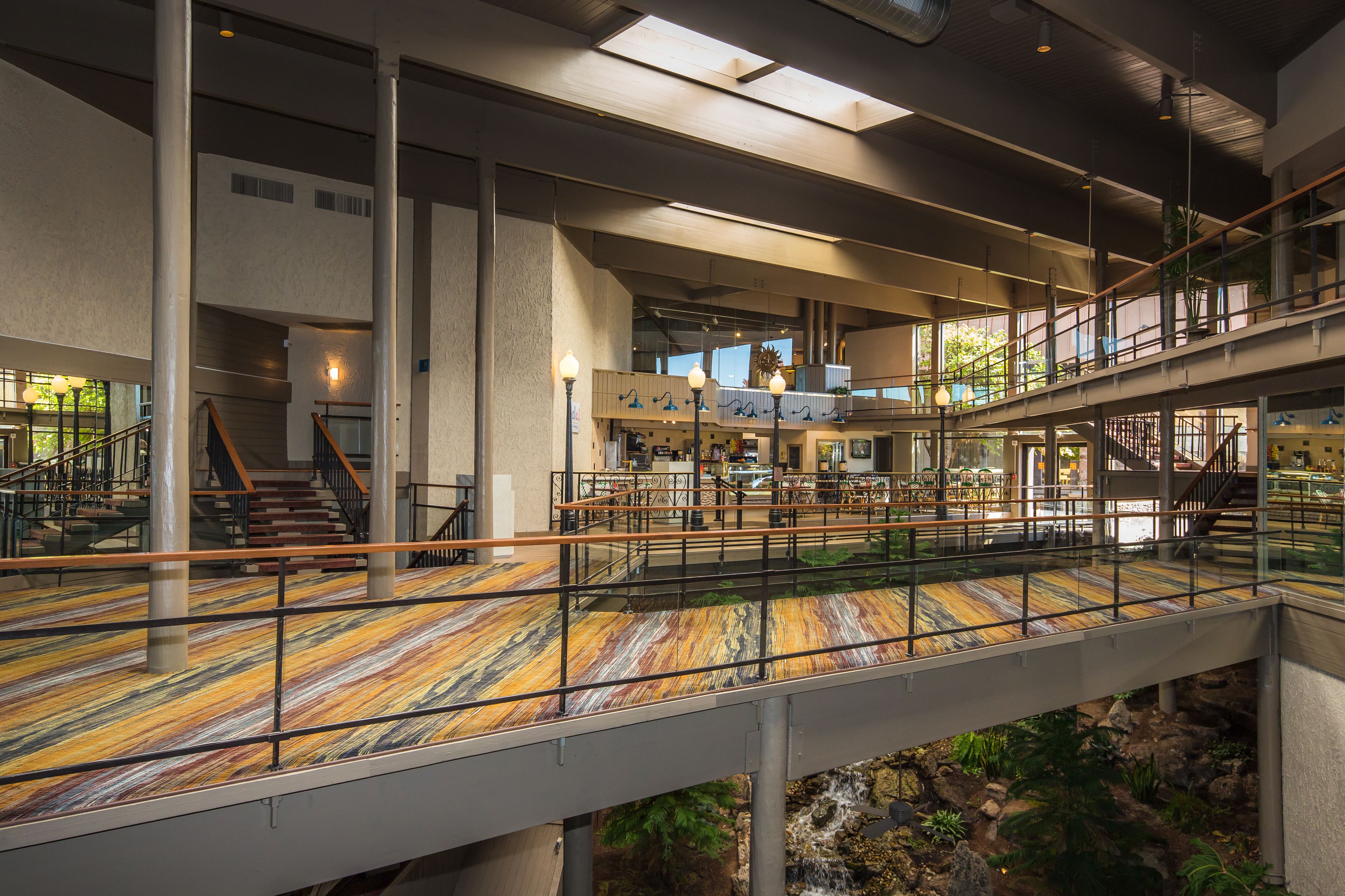 A spacious indoor area with multiple levels, a central staircase, and a glass bridge over a water feature.