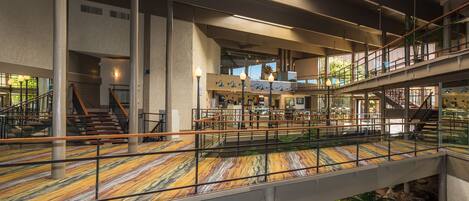 A spacious indoor area with multiple levels, a central staircase, and a glass bridge over a water feature.