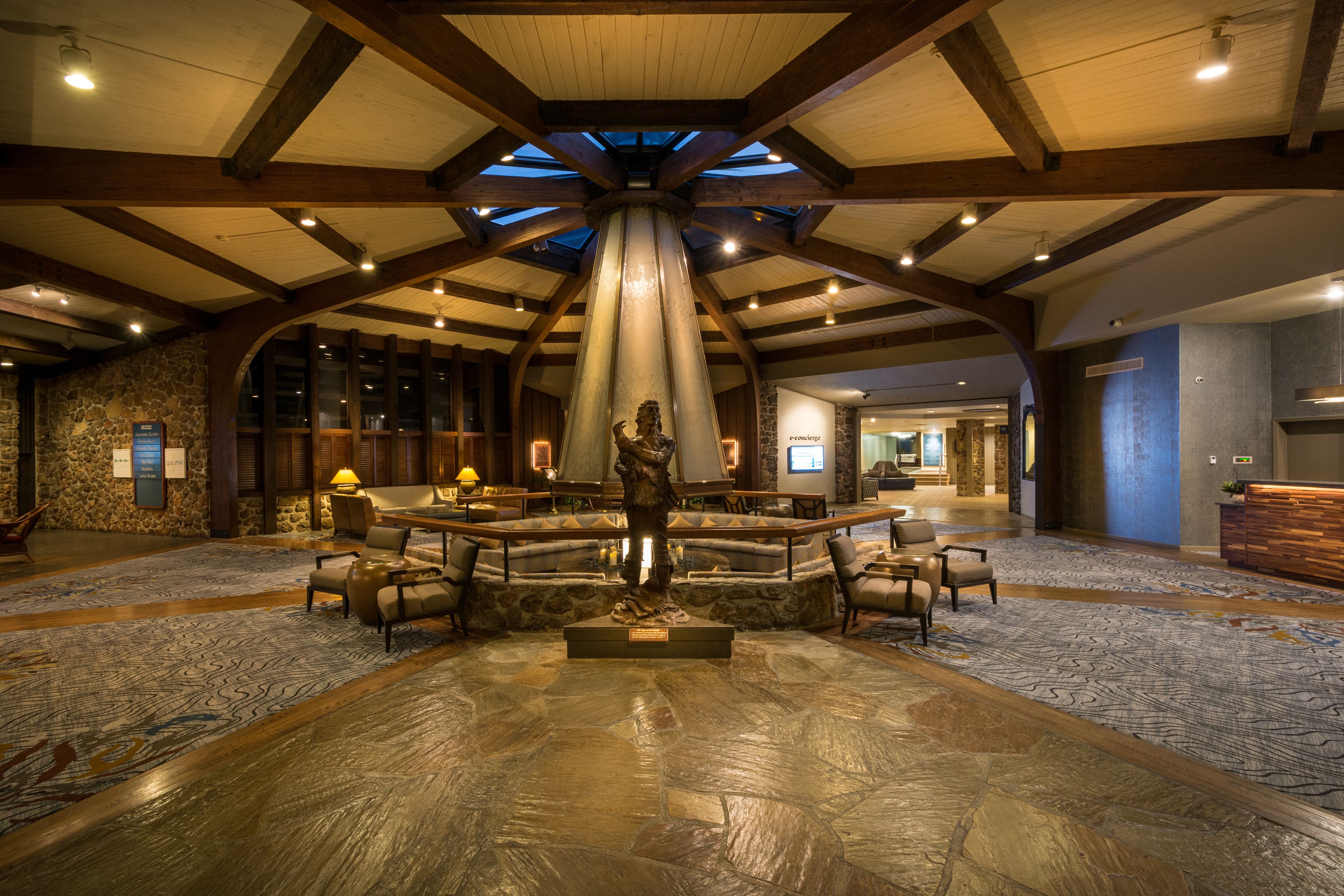 A lobby with a stone floor, wooden beams, a central statue, and seating areas.