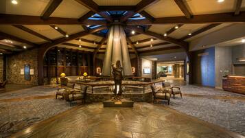 A lobby with a stone floor, wooden beams, a central statue, and seating areas.