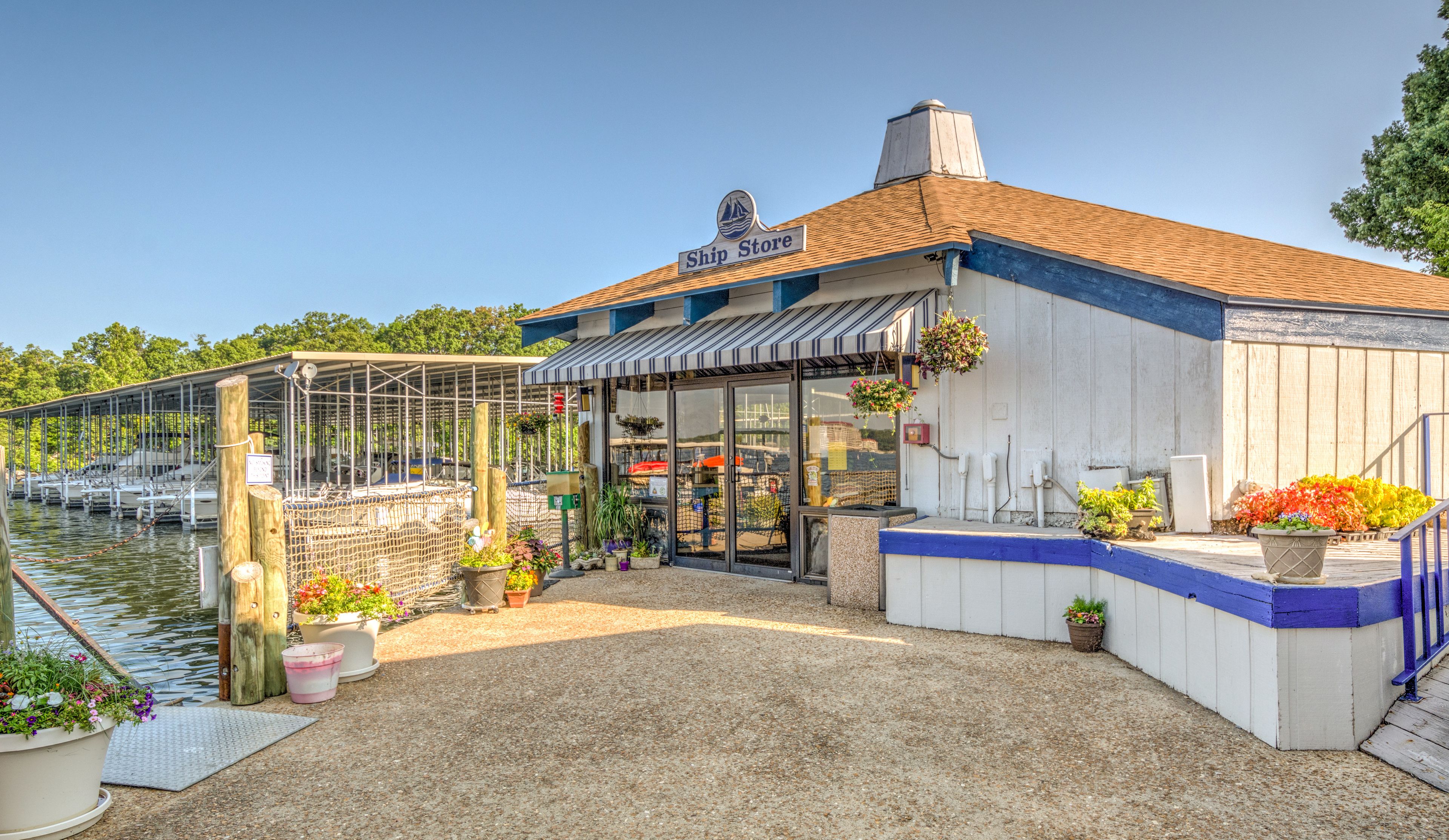 A waterfront building with a sign reading "Ship Store," featuring a covered dock area, potted plants, and a gravel ground.