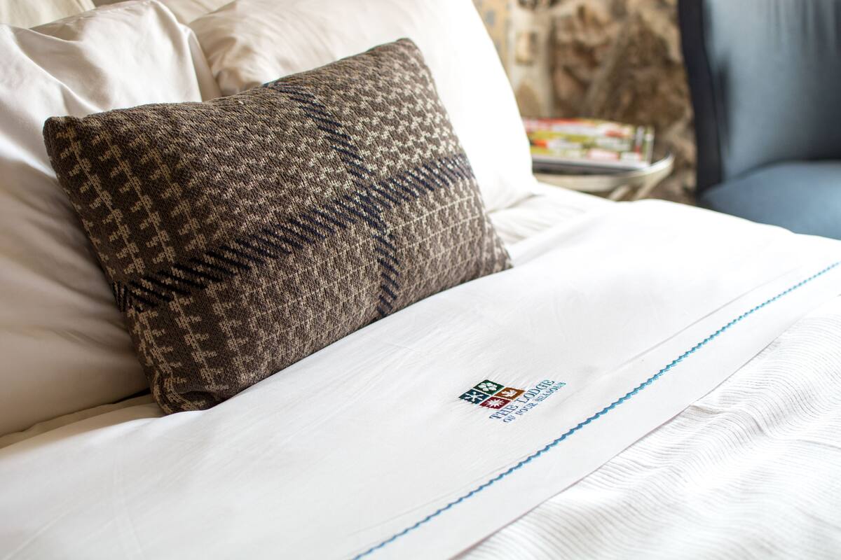 Un lit bien fait, avec un oreiller à motifs et un drap blanc orné d’un logo.