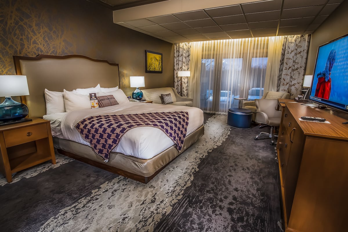 Une chambre d’hôtel avec un grand lit, deux tables de chevet, un bureau, une chaise, une télévision et une fenêtre avec des rideaux.
