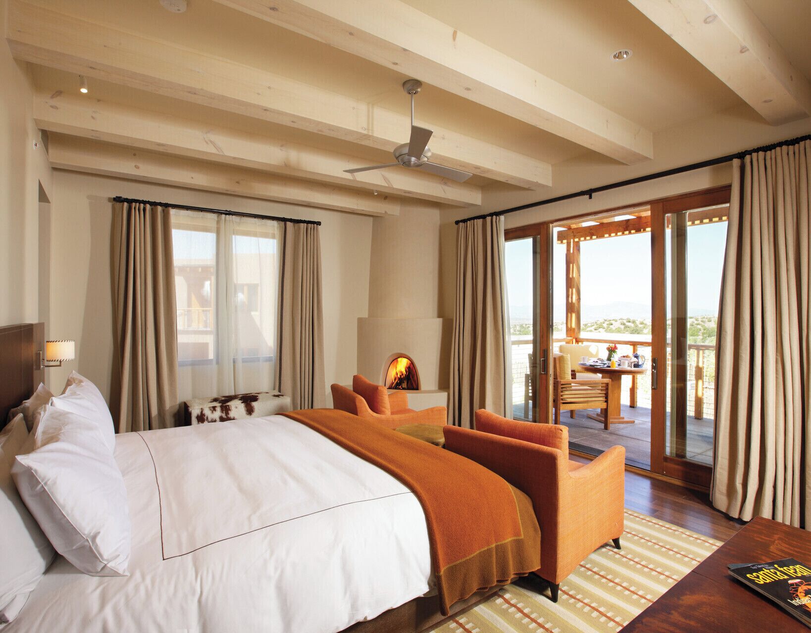 A hotel room with a bed, a sofa, a table with a chair, a fireplace, and a balcony with curtains.