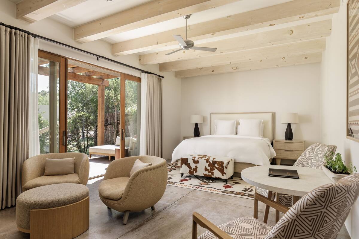 A modern bedroom with a large bed, two bedside tables, a ceiling fan, and a view of the outdoors.