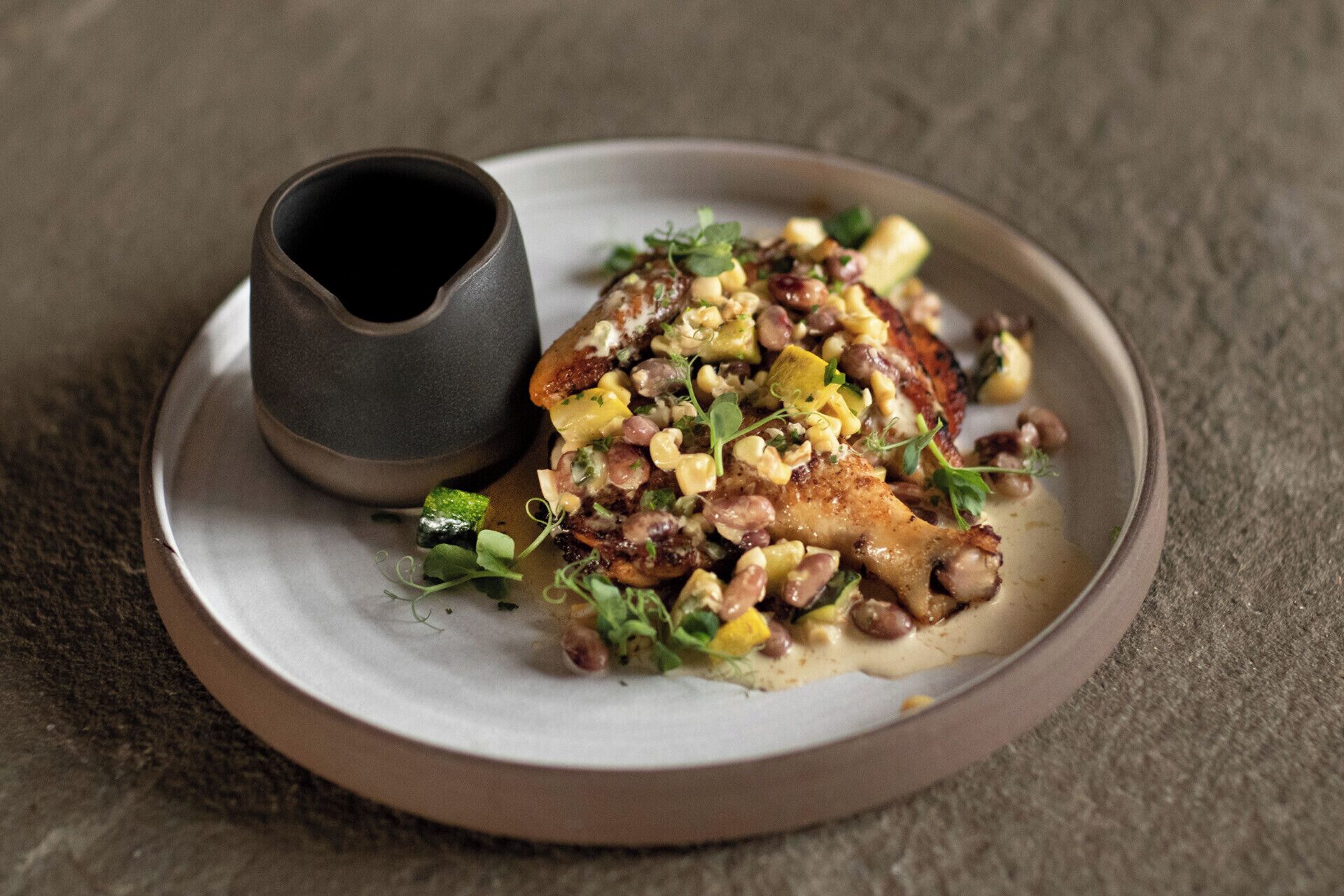 Une assiette contenant un morceau de poulet grillé, des haricots et des légumes, accompagnée d’une petite tasse.