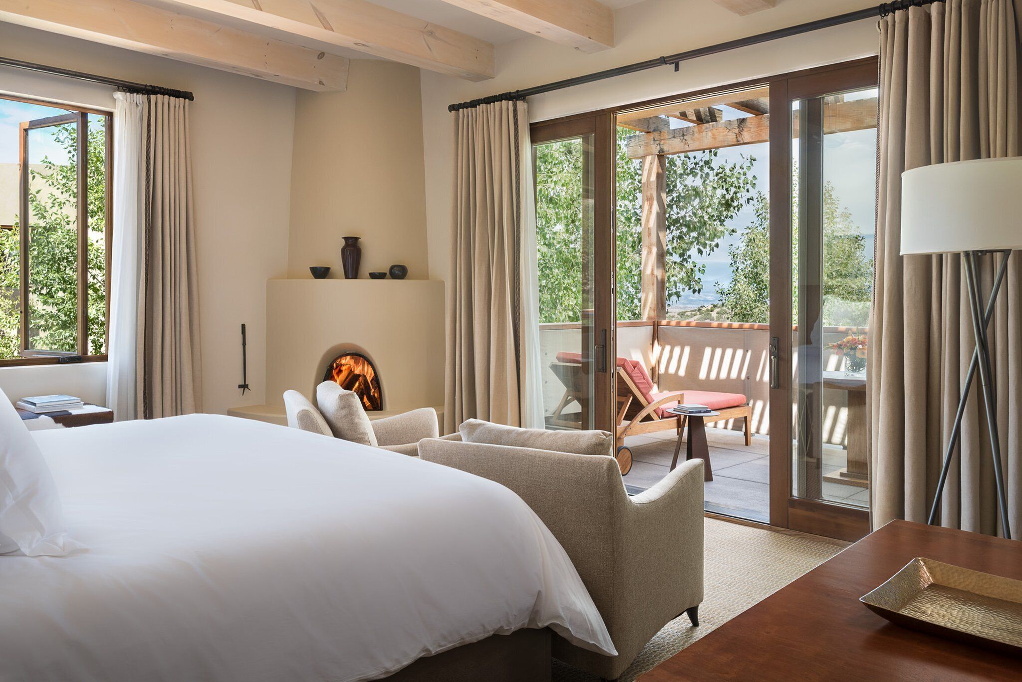 A hotel room with a large bed, two armchairs, a fireplace, and a balcony with a table and chairs.