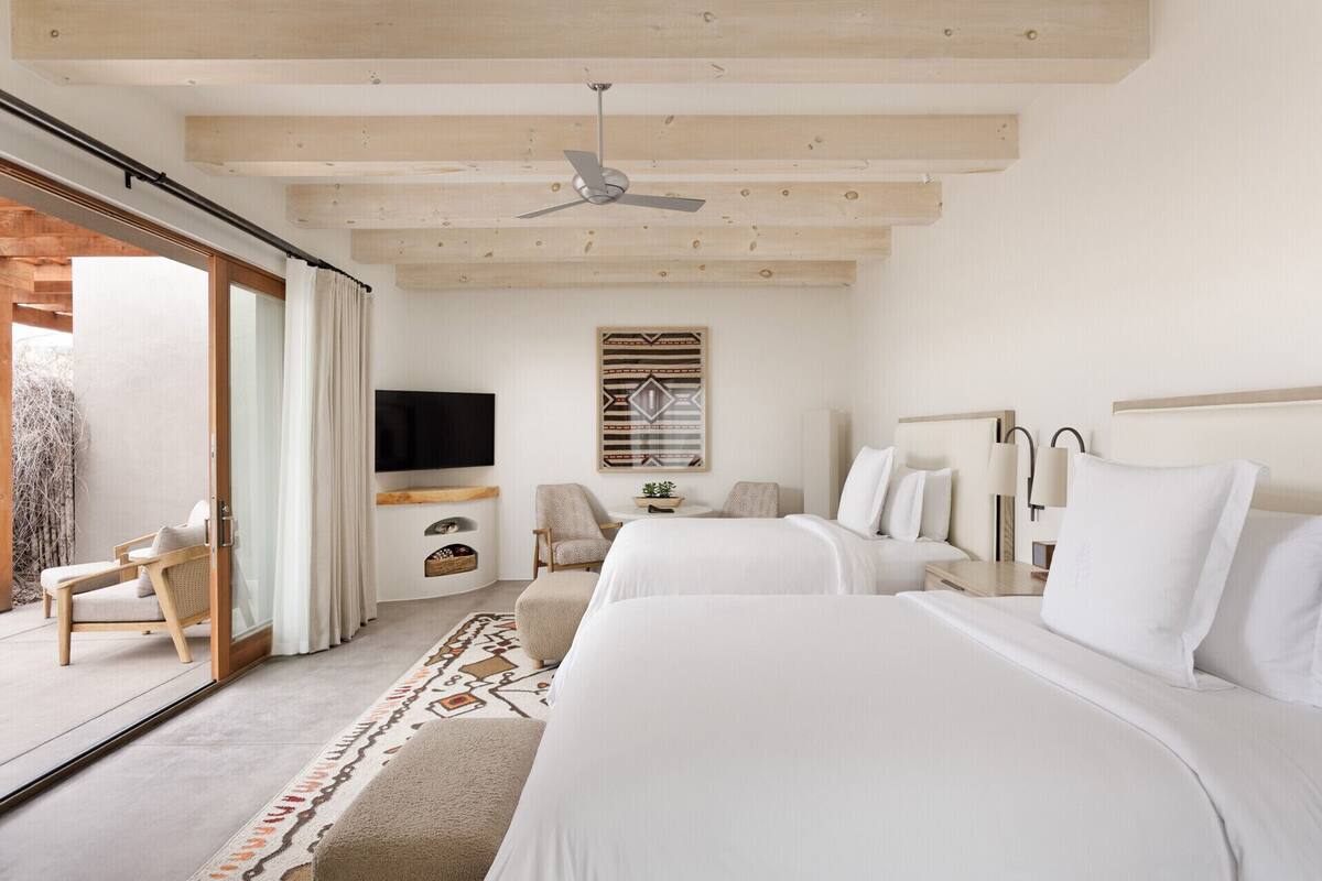 A hotel room with a large bed, a smaller bed, a TV mounted on the wall, a ceiling fan, and a sliding glass door leading to an outdoor area.