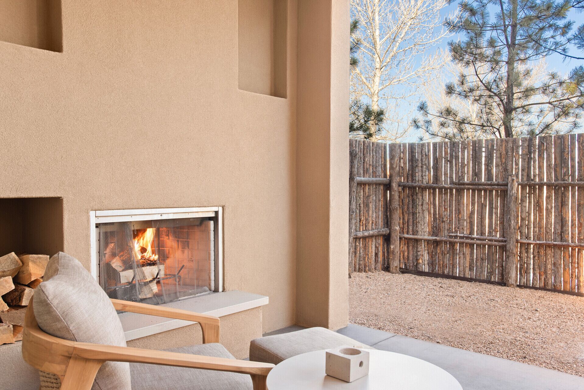 Un espace extérieur moderne aménagé avec des sièges, une cheminée, des meubles en bois et une vue sur une clôture en bois et des arbres.