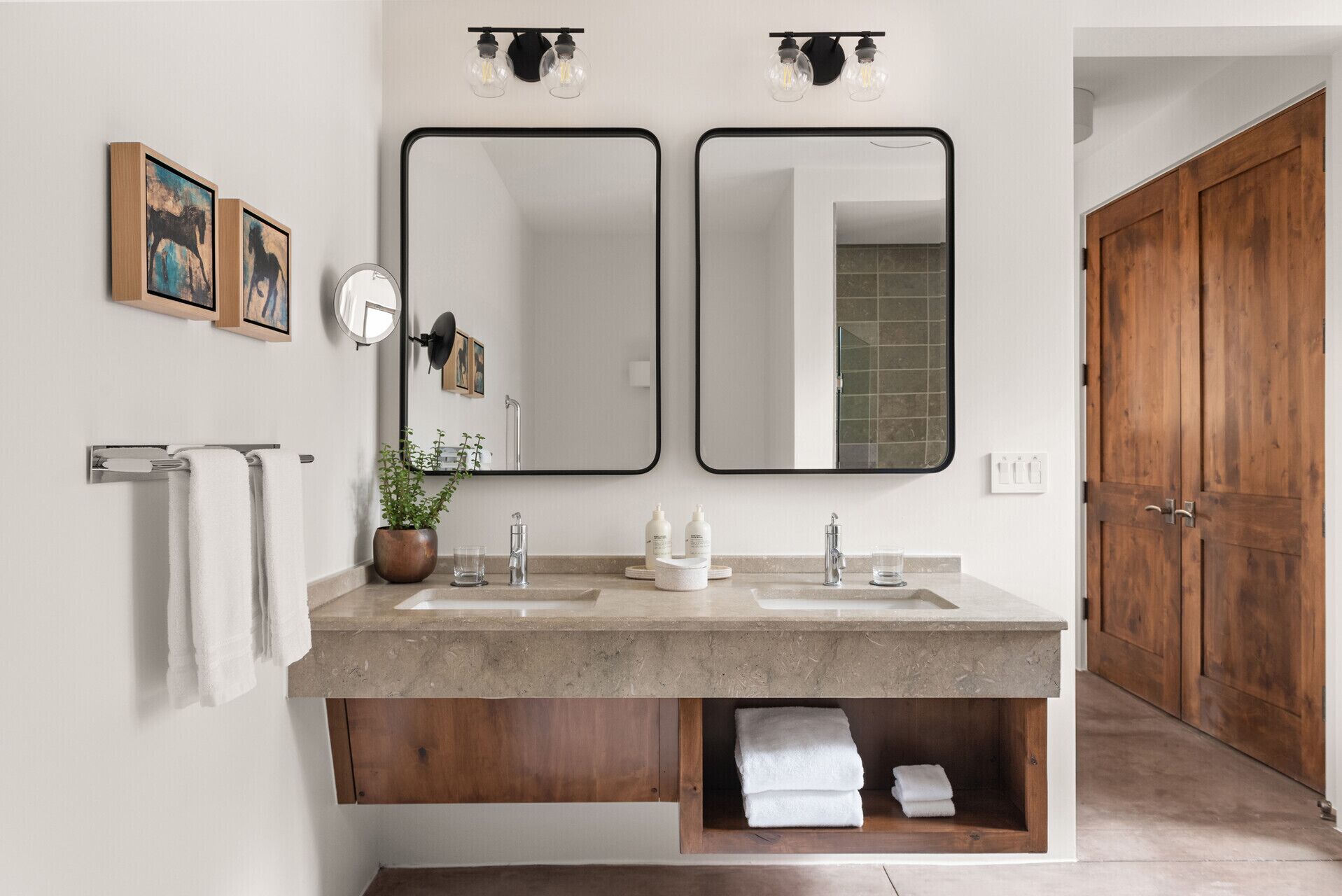 A modern bathroom with a double sink vanity, a large mirror, and a wooden door.