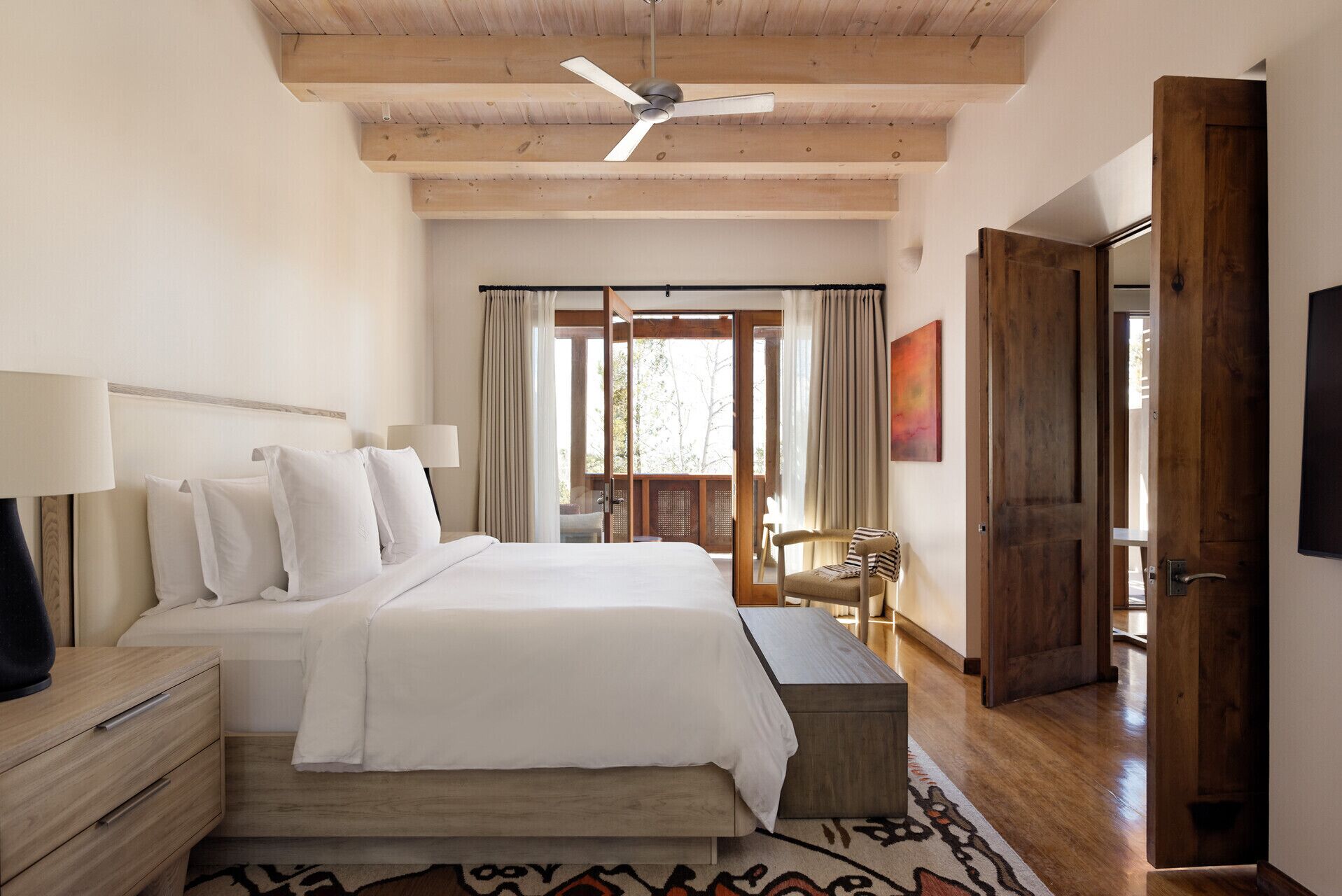 A bedroom with a bed, bedside tables, a ceiling fan, a window with curtains, a chair, and a door.