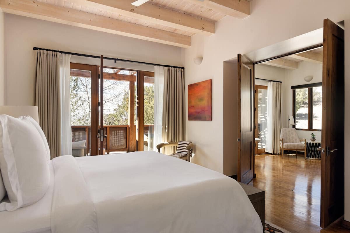A bedroom with a large bed, a chair, a painting, and a view of the outdoors.