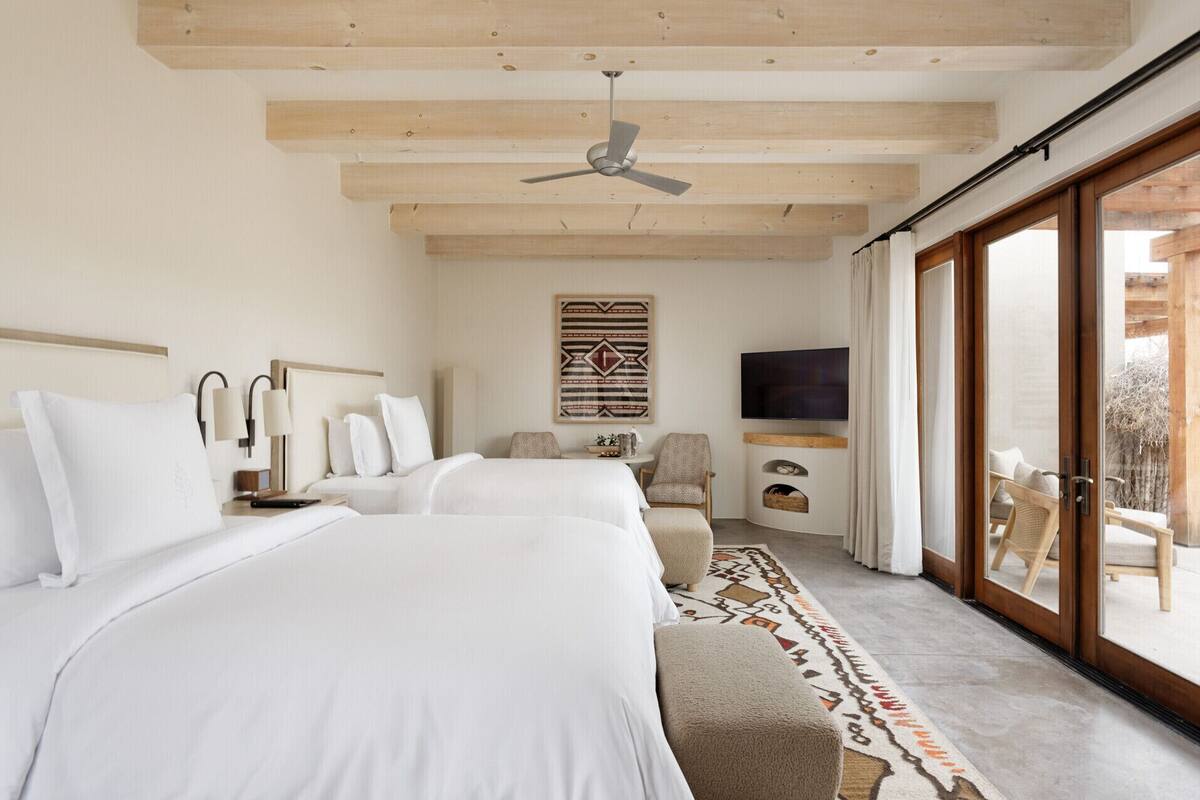 A modern hotel room with two beds, a ceiling fan, a flat-screen TV, and a large sliding glass door to the outside.