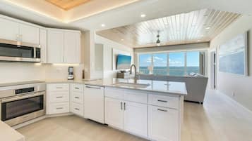 A modern kitchen with built-in appliances, a large island, and a view of the sea.