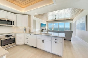 A modern kitchen with built-in appliances, a large island, and a view of the sea.
