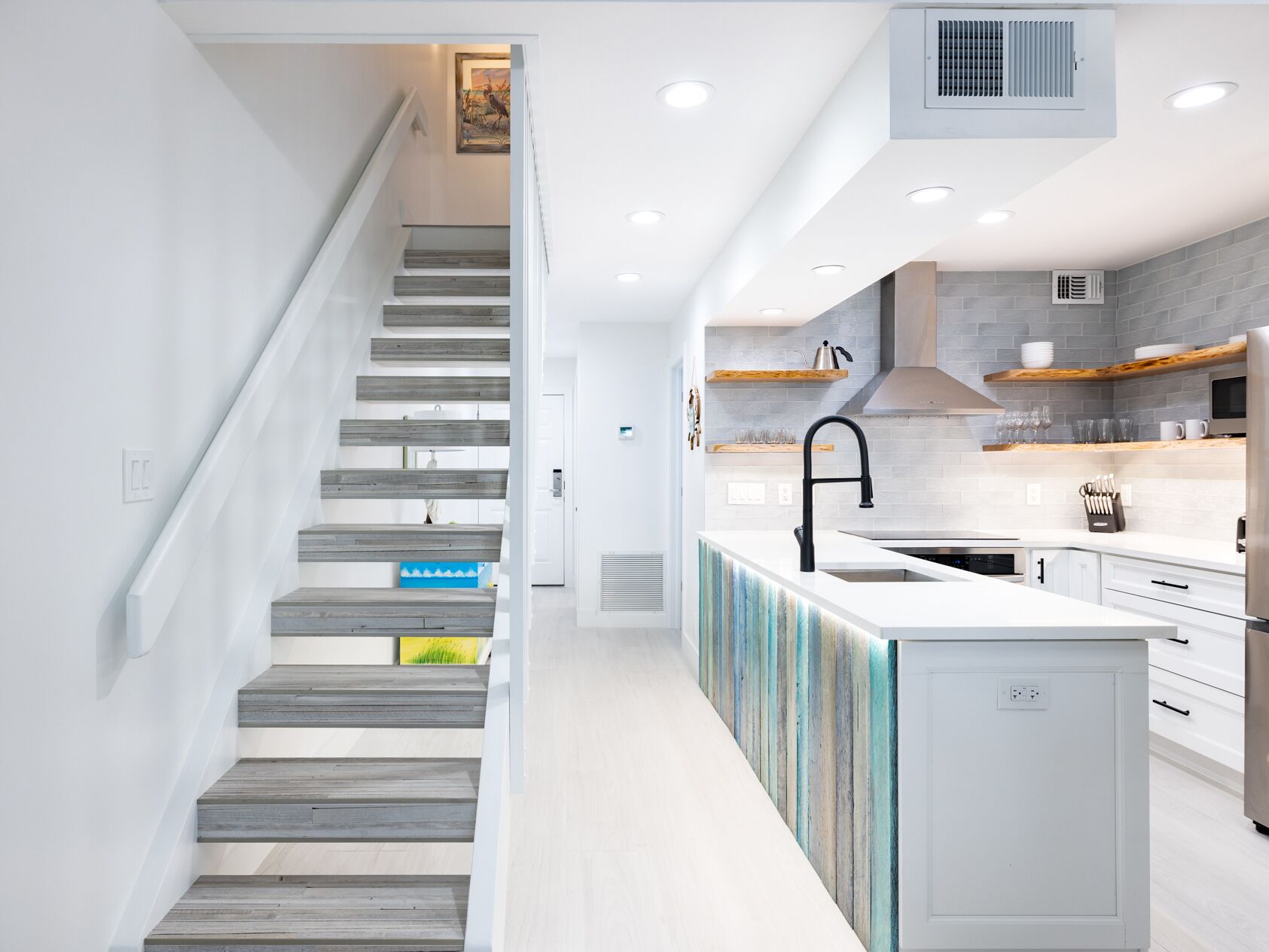 Una cocina moderna con una isla central, muebles blancos y una escalera de madera.