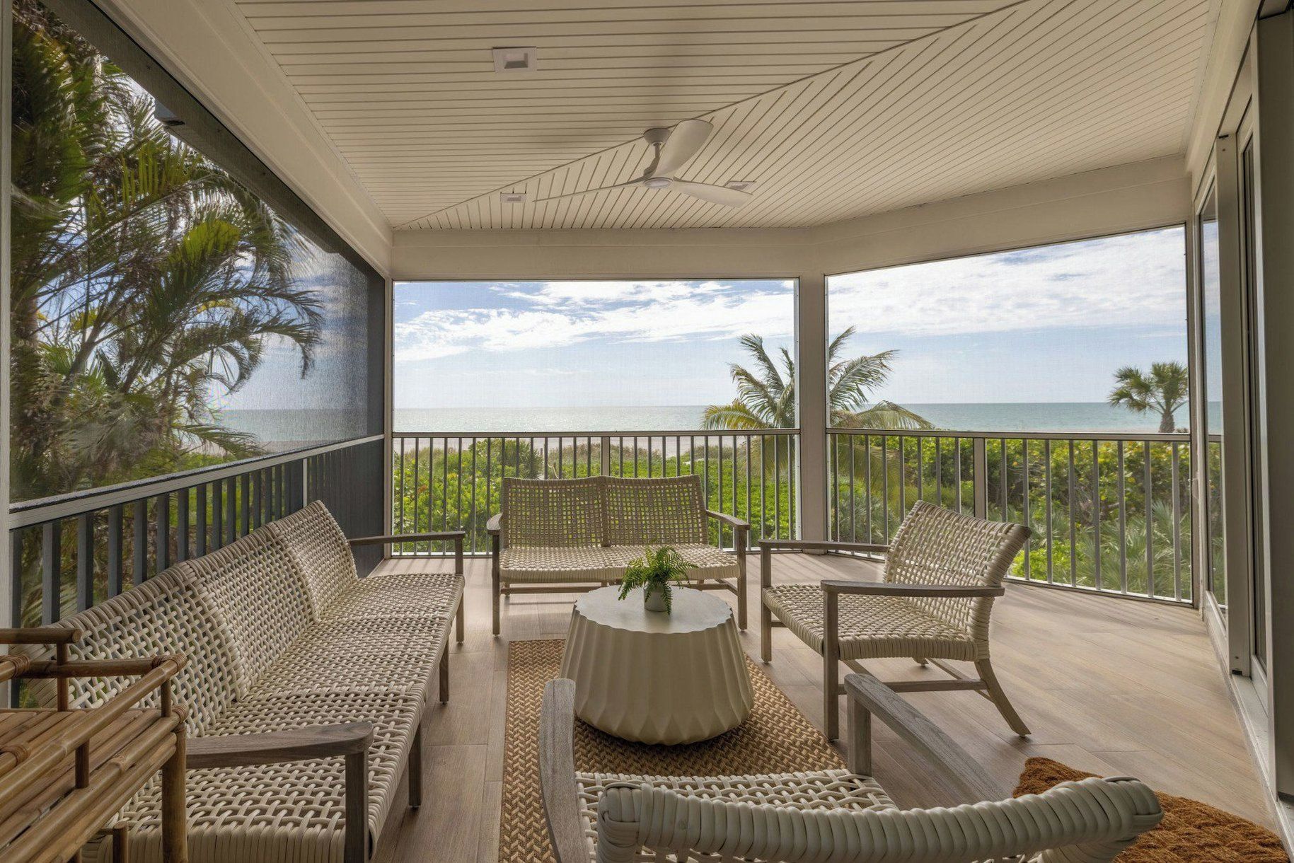 A balcony with wicker furniture, a round table, and a view of the ocean.