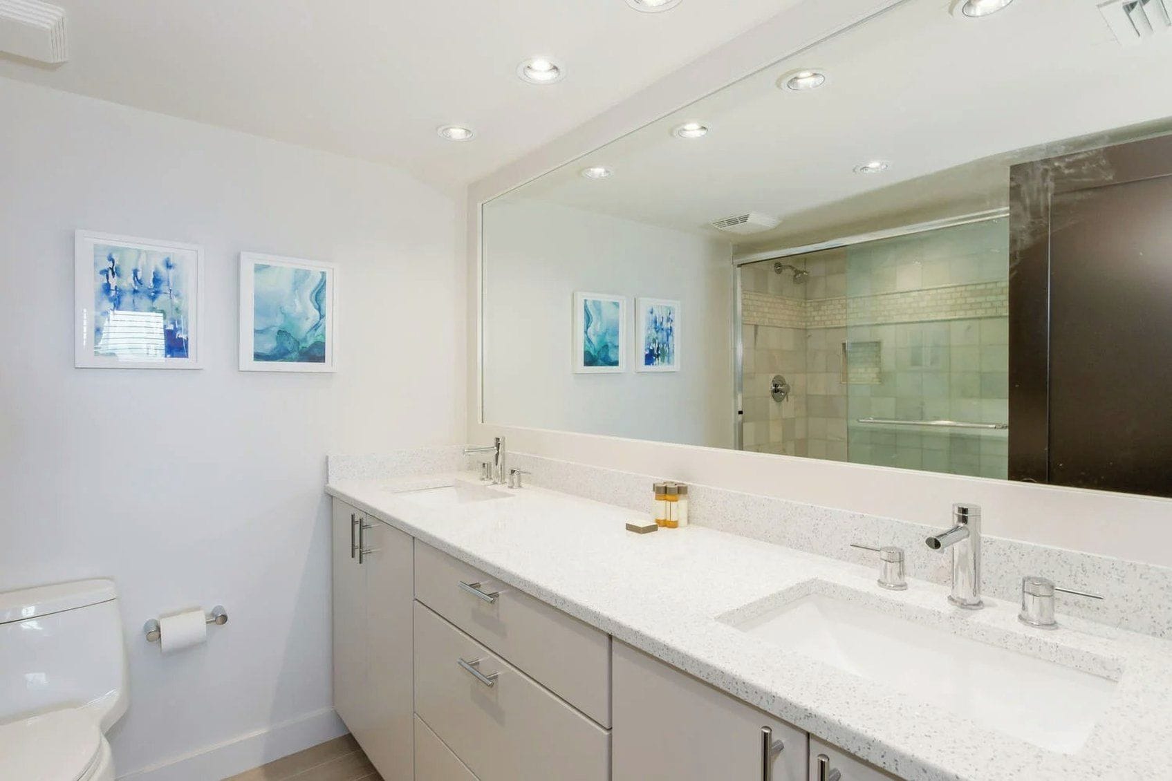 A modern bathroom with a large mirror, two sinks, and a shower area.