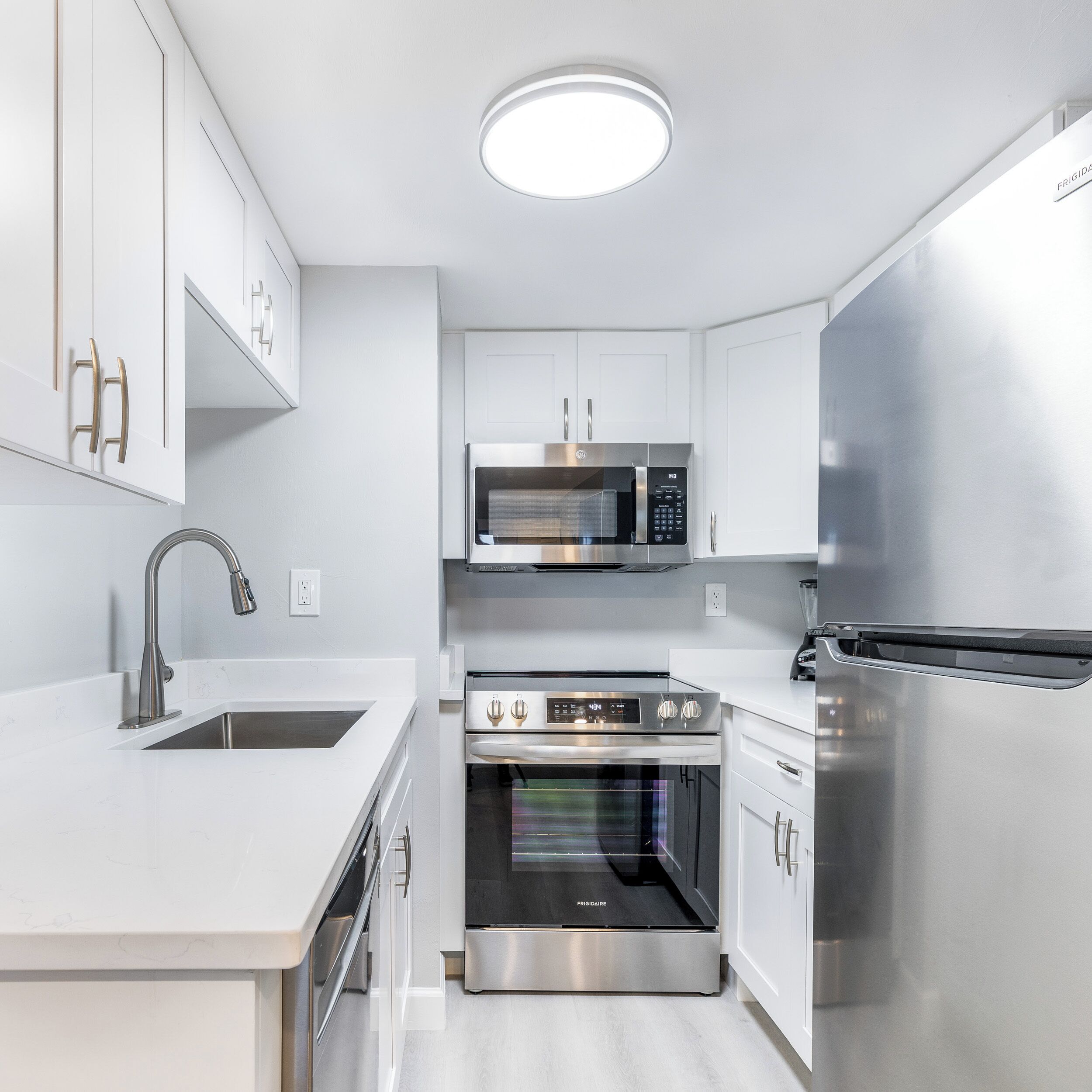 Una cocina moderna con armarios blancos, electrodomésticos de acero inoxidable, horno empotrado y microondas.
