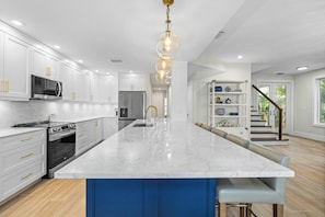 A modern kitchen with white cabinetry, a large marble island, and a central light fixture. - South Seas (Captiva)