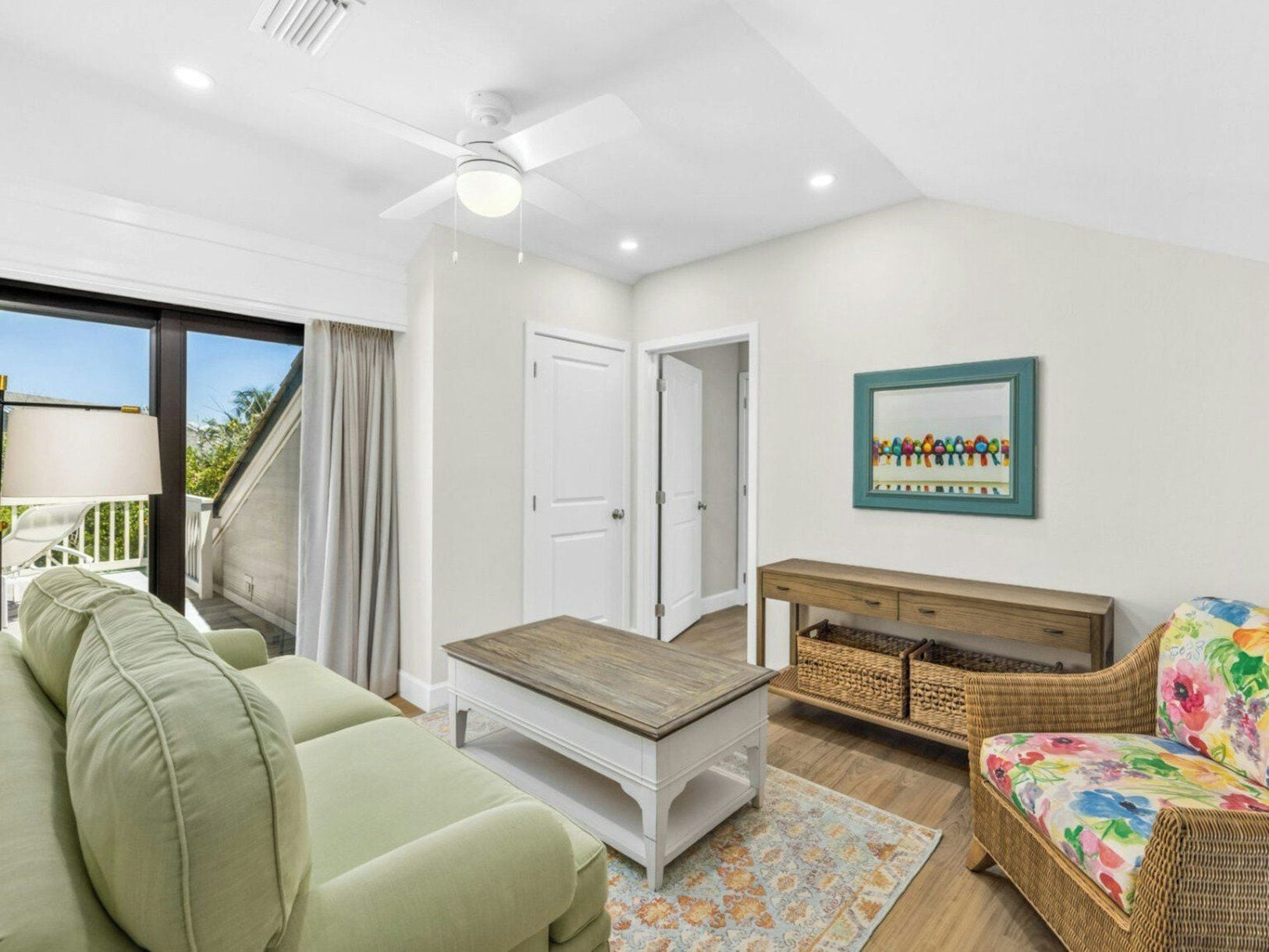A modern living room with a sofa, a coffee table, a wicker chair, a framed picture on the wall, and a ceiling fan.