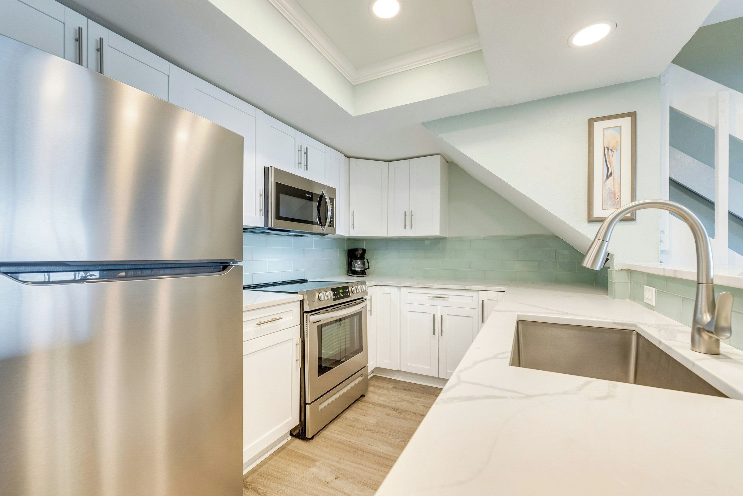 A modern kitchen with stainless steel appliances, white cabinetry, and a light green backsplash.
