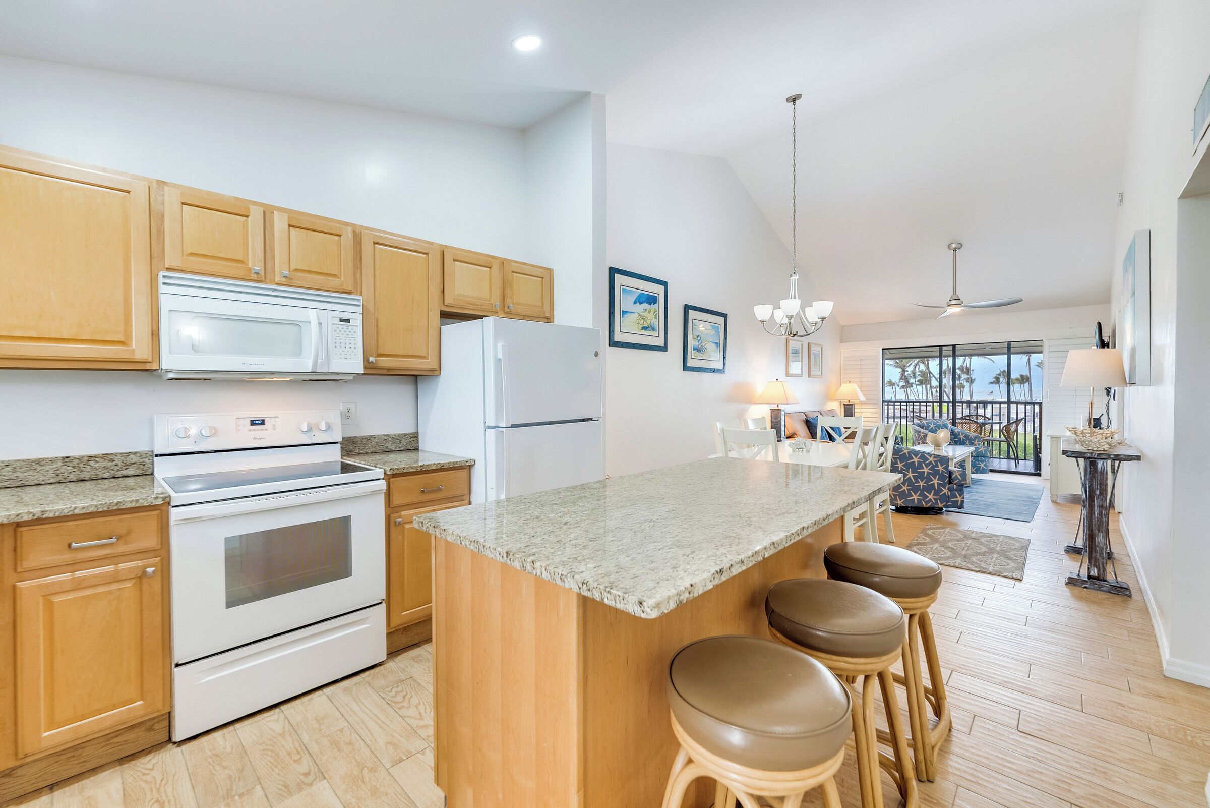A kitchen with wooden cabinets, a built-in oven, a microwave, and a granite countertop. There are three stools at the island.