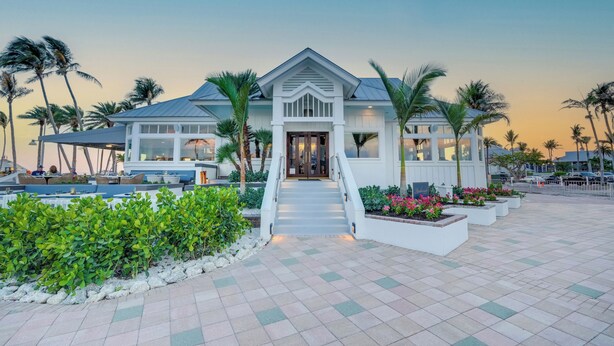 A beachfront hotel with a central entrance, outdoor seating, and palm trees. - South Seas (Captiva)