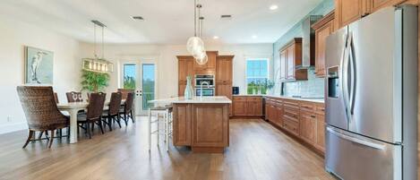 A modern kitchen with wooden cabinets, a stainless steel refrigerator, and a dining area with wicker chairs.