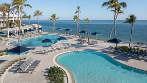 A resort pool area with multiple sun loungers and umbrellas, surrounded by palm trees and a view of the ocean. - South Seas (Captiva)