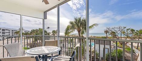 Un balcon avec une table et des chaises, donnant sur une plage et des palmiers.