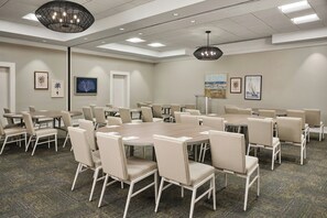 A conference room with multiple tables and chairs, a ceiling light fixture, and framed artwork on the walls. - South Seas (Captiva)
