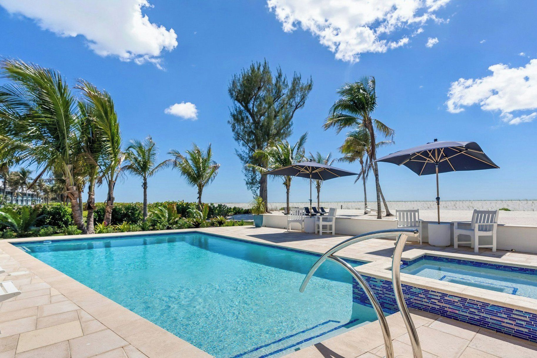 A swimming pool with lounge chairs and umbrellas, surrounded by palm trees and a clear sky.
