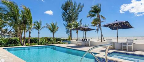 A swimming pool with lounge chairs and umbrellas, surrounded by palm trees and a clear sky.