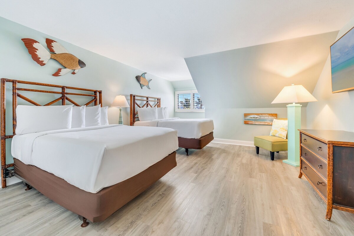 A bedroom with two beds, a dresser, a lamp, and wall art.