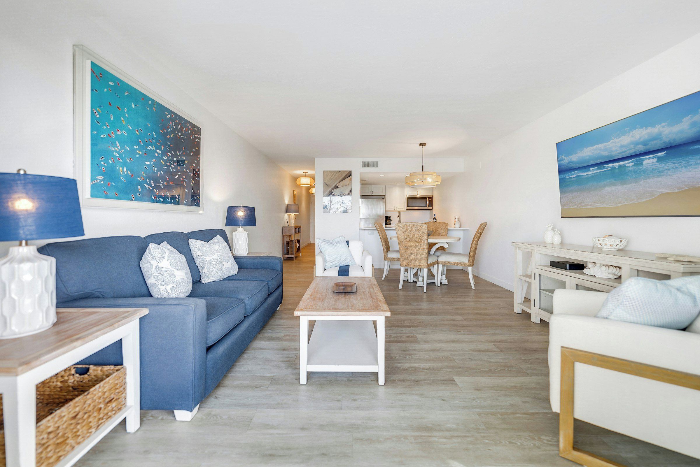 Un salon moderne avec un canapé bleu, des fauteuils blancs et un coin repas doté de chaises en osier.