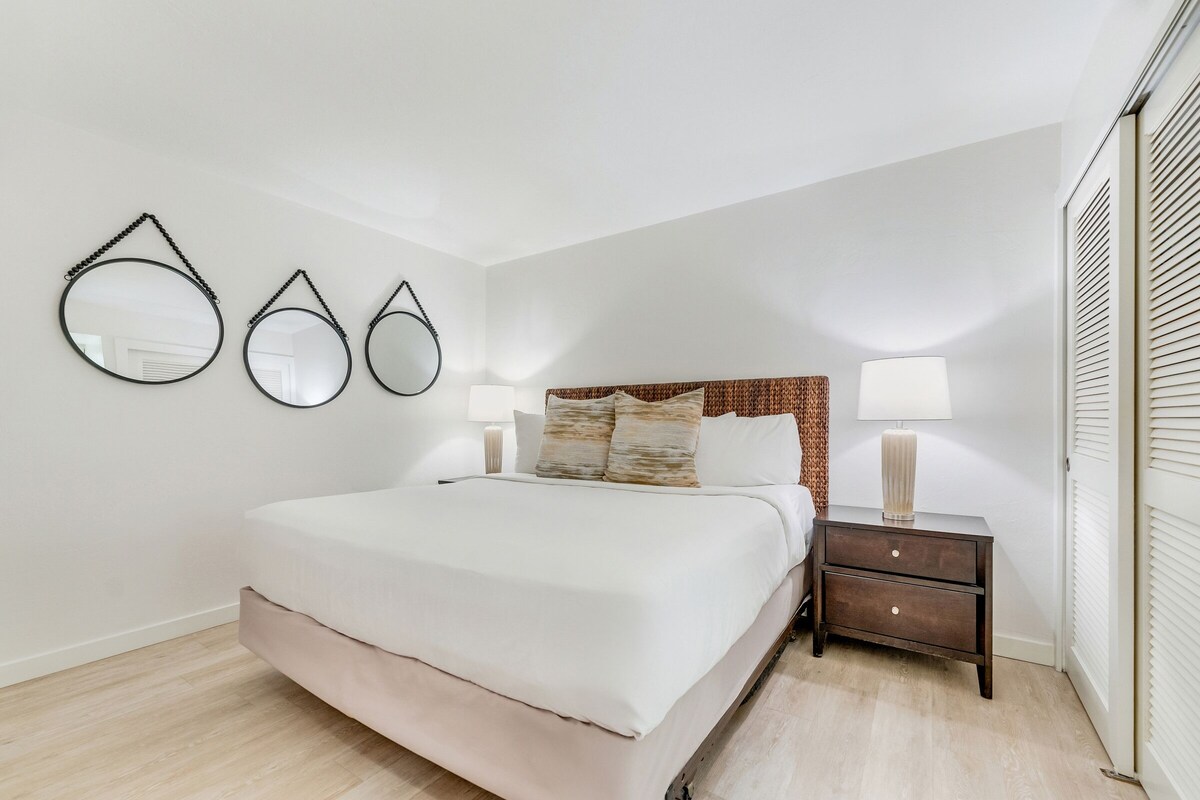 A bedroom with a large bed, two bedside tables with lamps, and three wall-mounted mirrors.