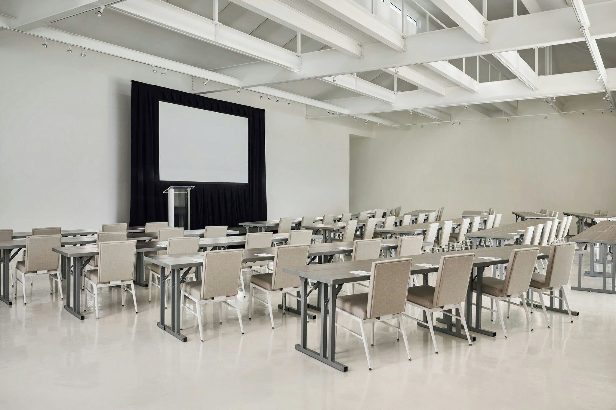 A conference room with a large screen, multiple tables, and chairs arranged for a meeting.