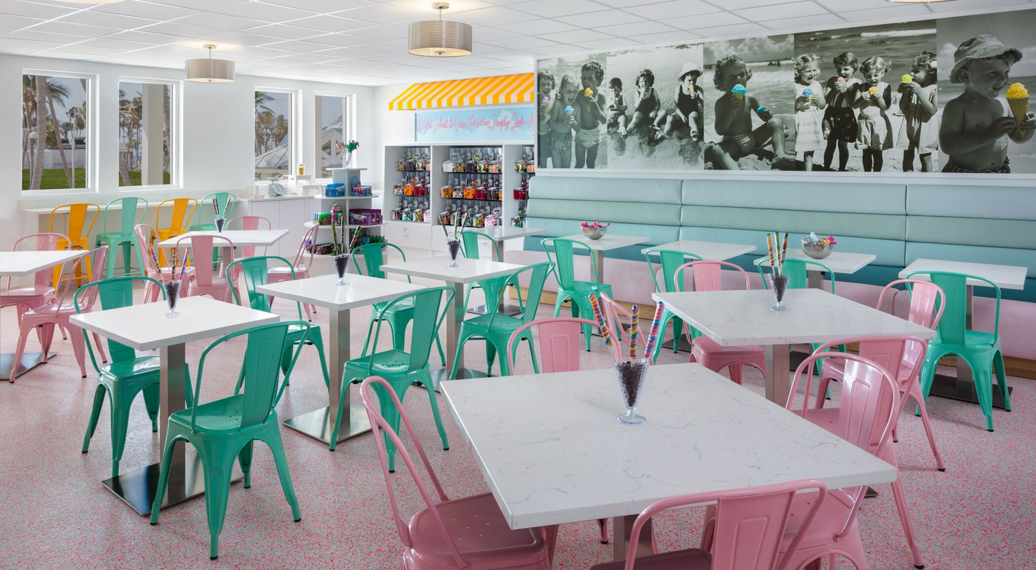 Ein lebhaftes Restaurant mit Türkis- und Rosa-Stühlen, weißen Tischen und einem Wandgemälde von Kindern.