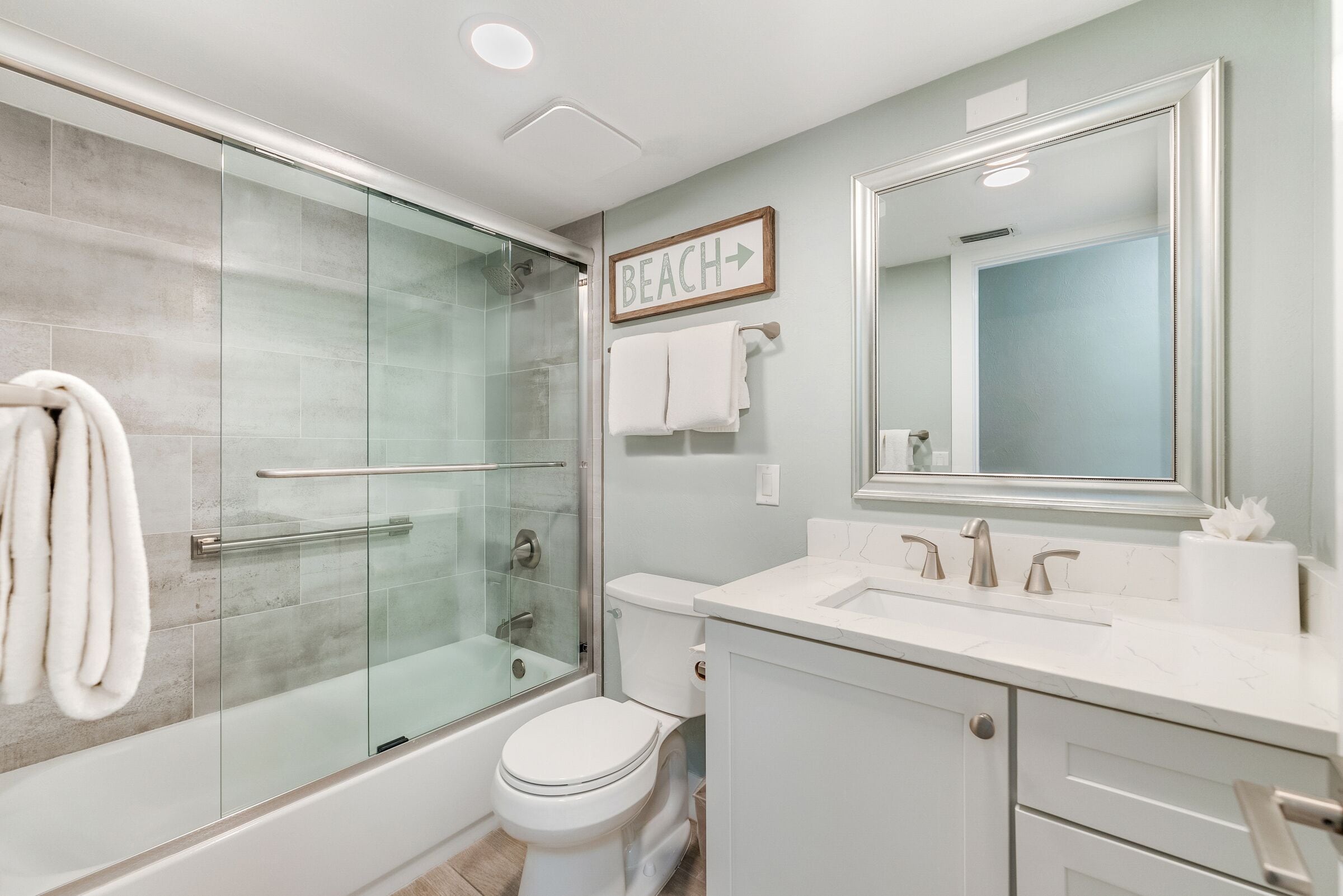 A modern bathroom with a glass-enclosed shower, a toilet, and a vanity with a mirror.