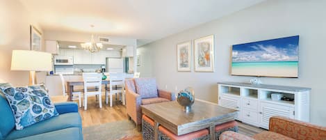 Un soggiorno moderno con un divano, un tavolino e cuscini decorati. Si intravede sullo sfondo un'area pranzo con un tavolo e sedie bianche.