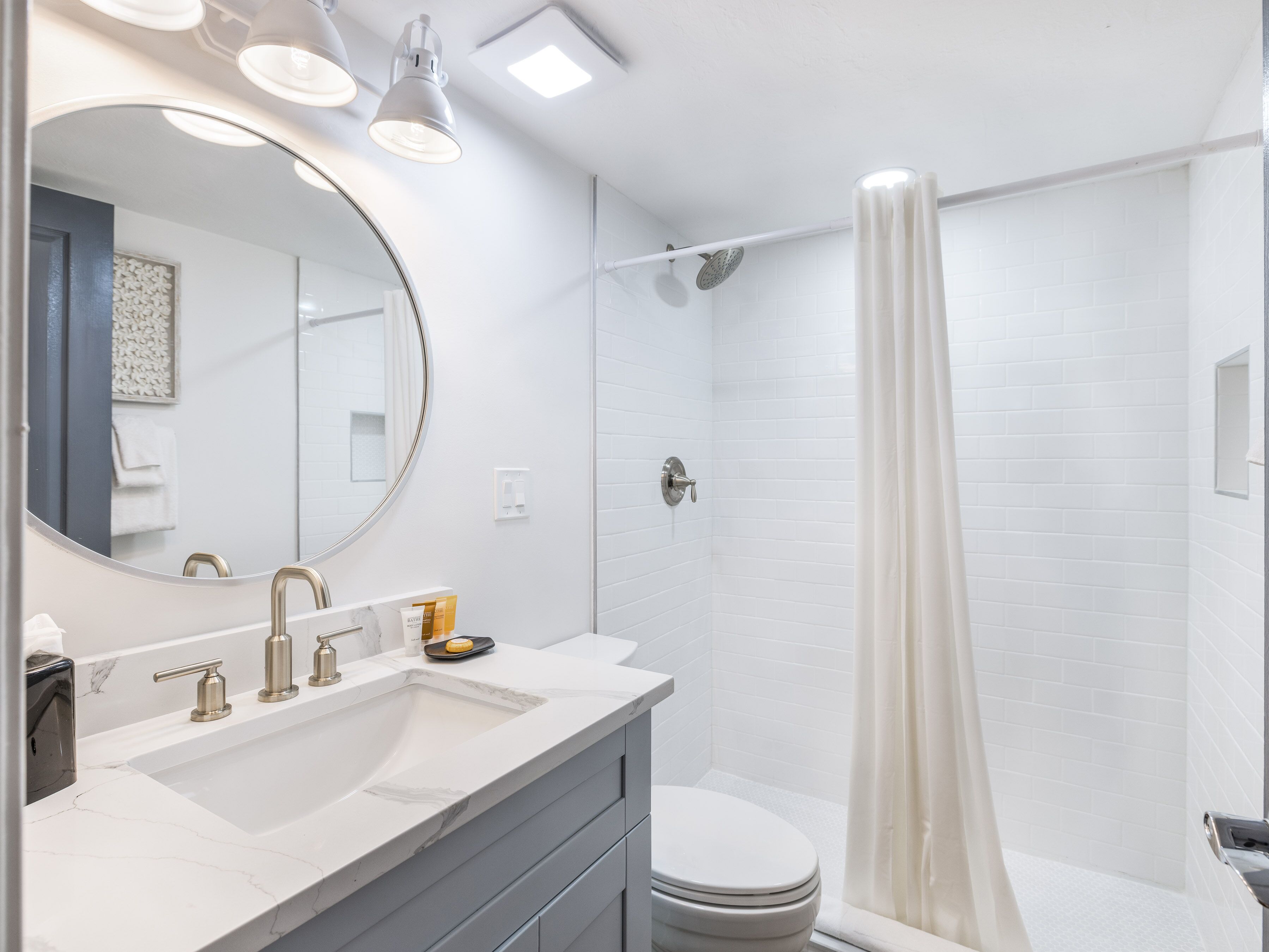 A modern bathroom with a white vanity, a round mirror, a shower with a curtain, and a toilet.