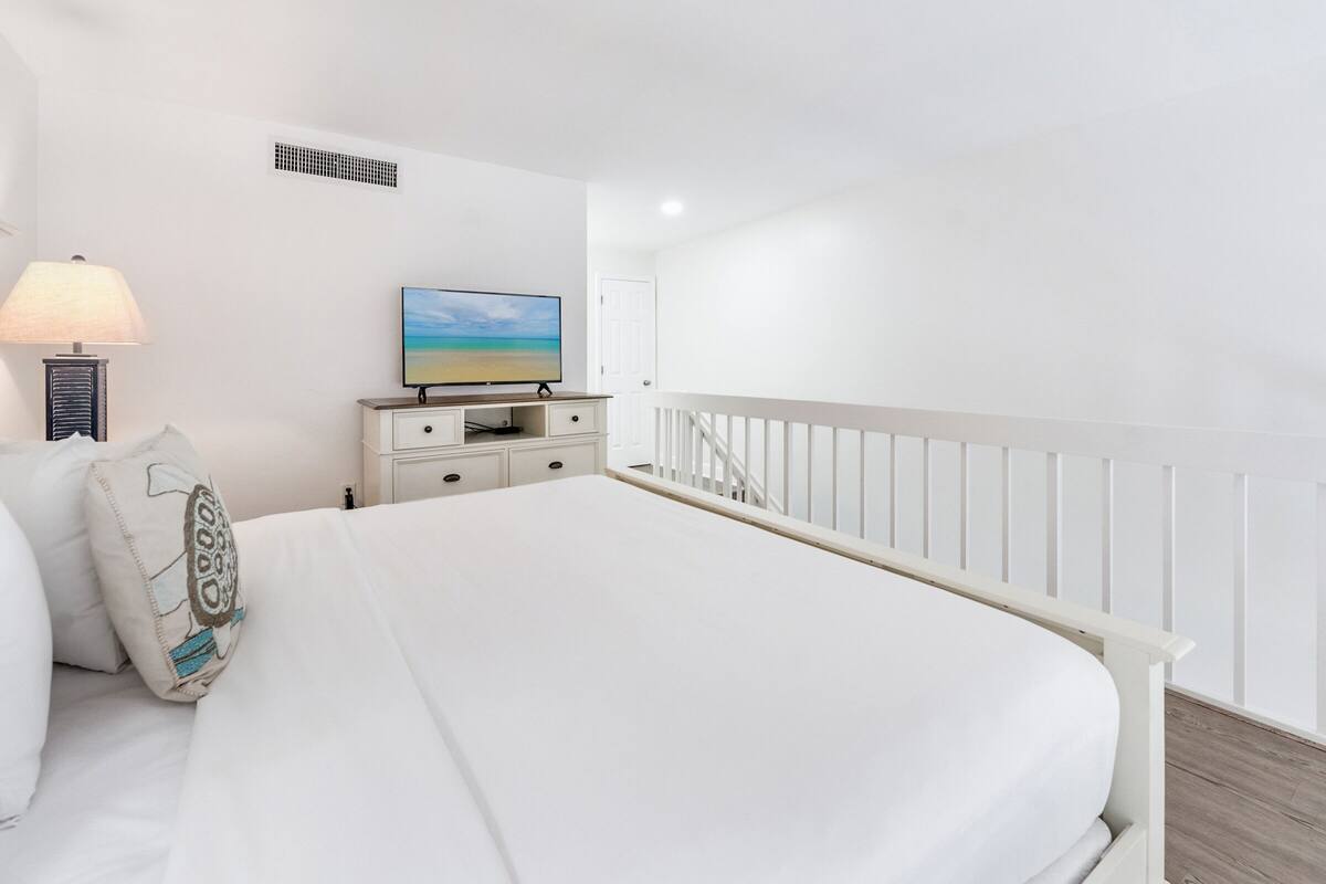 Une chambre à coucher avec un lit, une table de chevet, une lampe, un téléviseur et une balustrade blanche.