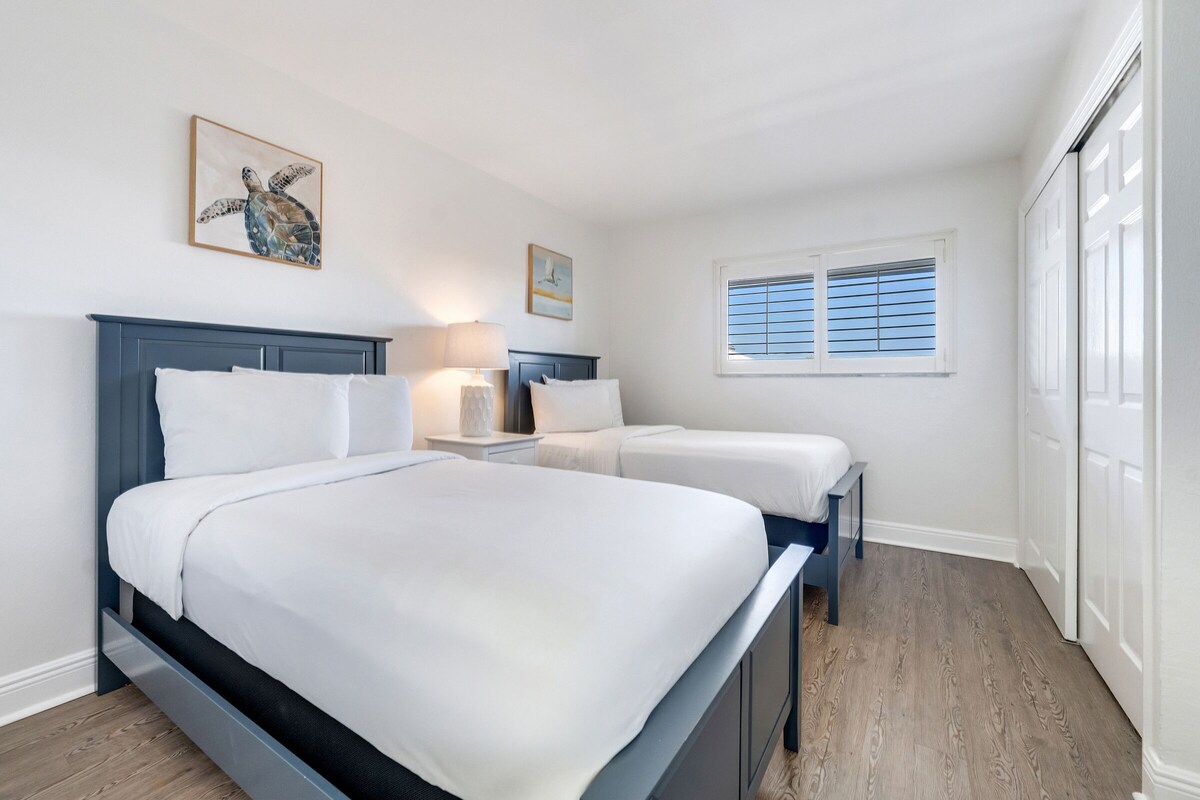A bedroom with a large bed, two bedside tables, and a window with blinds.