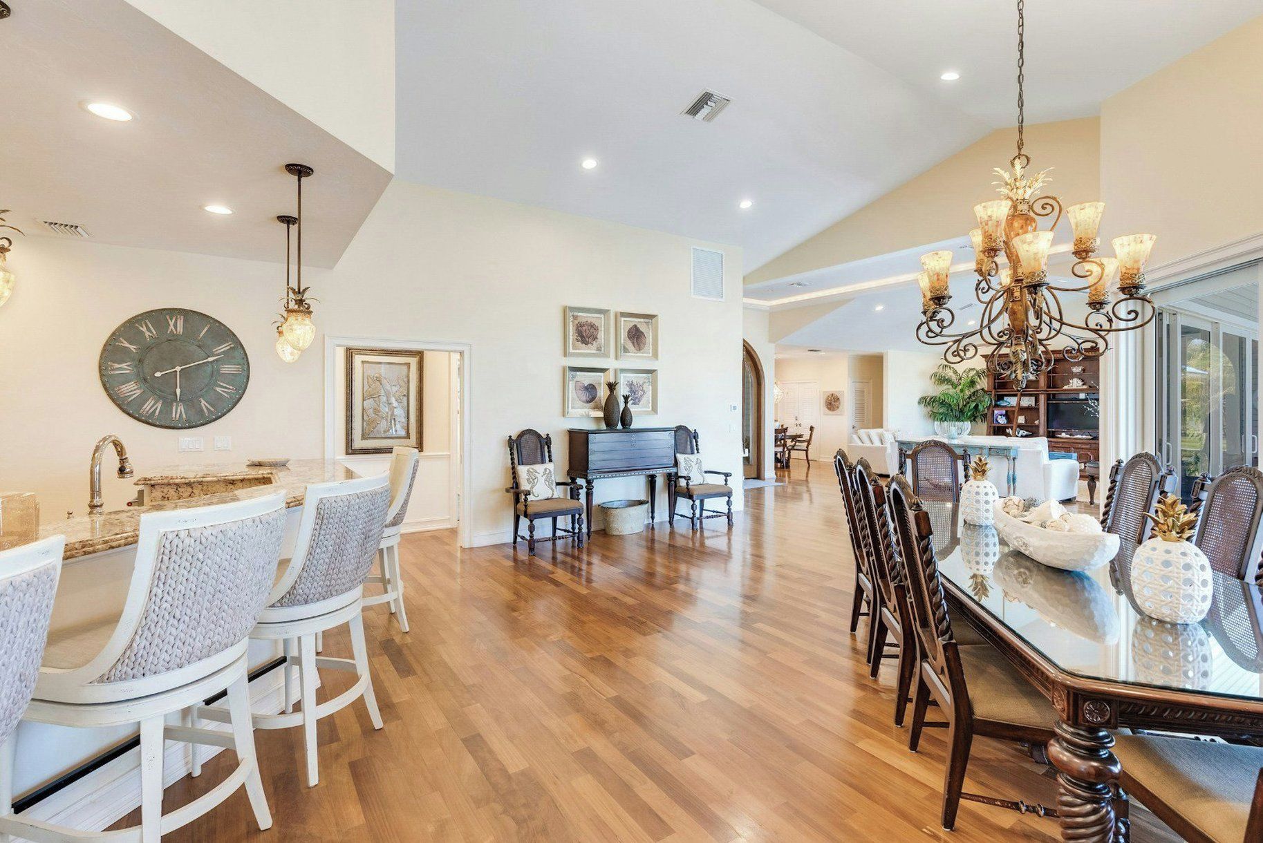 A spacious dining area with a wooden floor, a large round clock, and a chandelier.