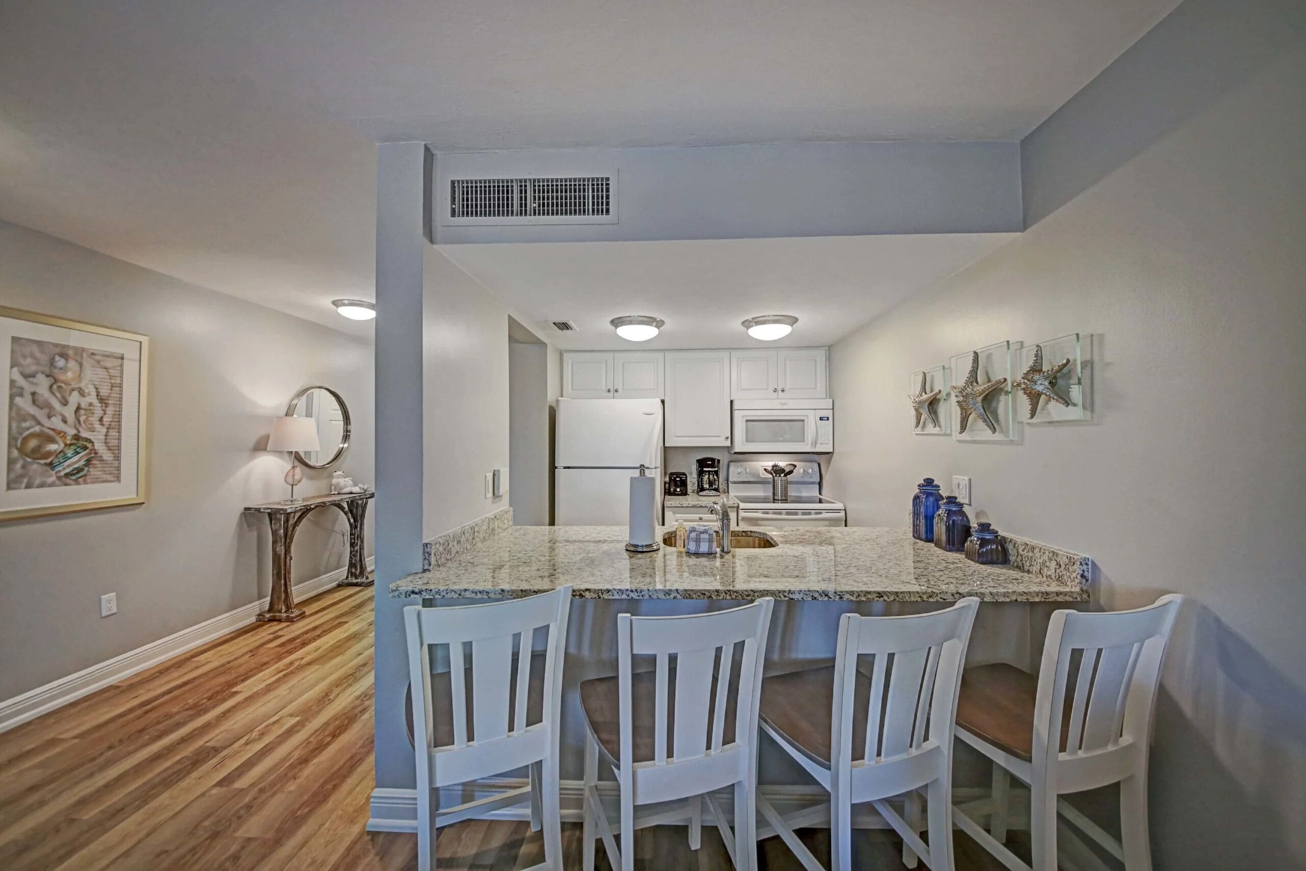 A modern kitchen with white cabinets, a granite countertop, and a dining area with four white chairs.